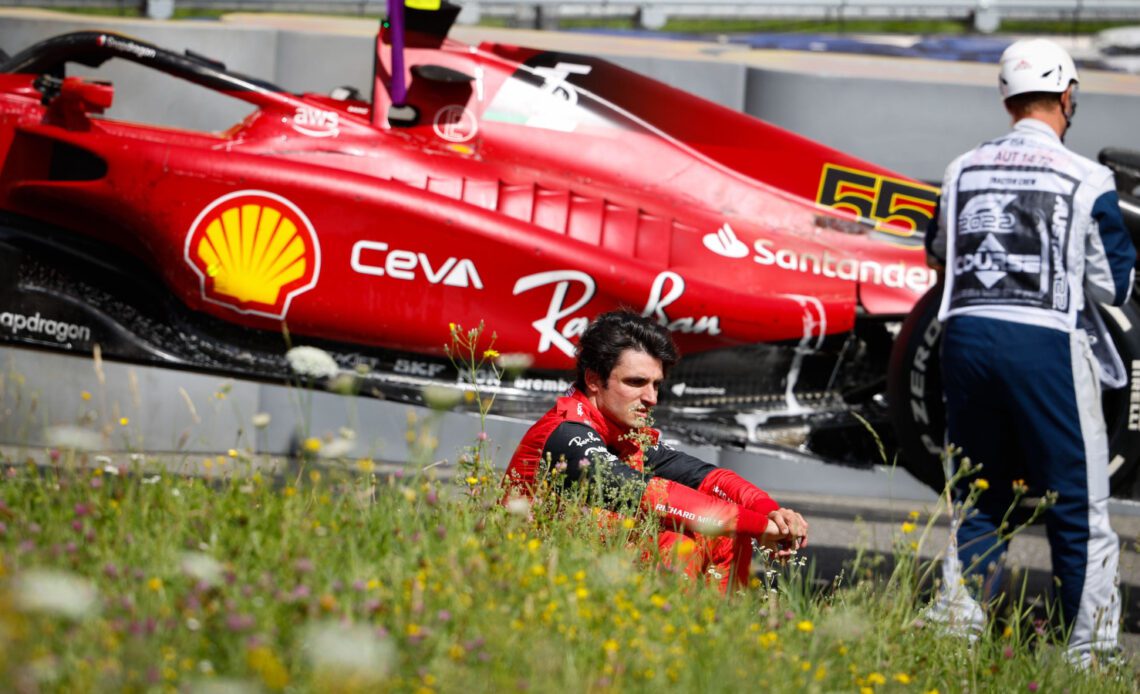 Carlos Sainz sitting on the grass, his retired Ferrari behind him. Austria July 2022