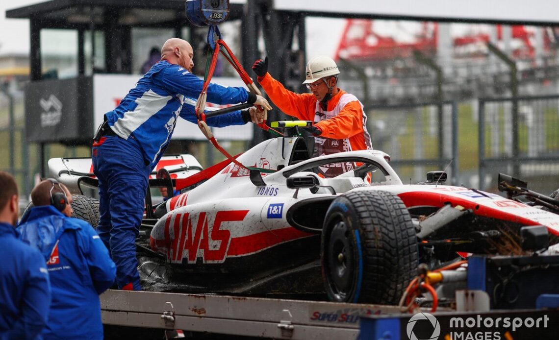 Mechanics and marshals unload the damaged car of Mick Schumacher, Haas VF-22, from a flat bed truck after FP1
