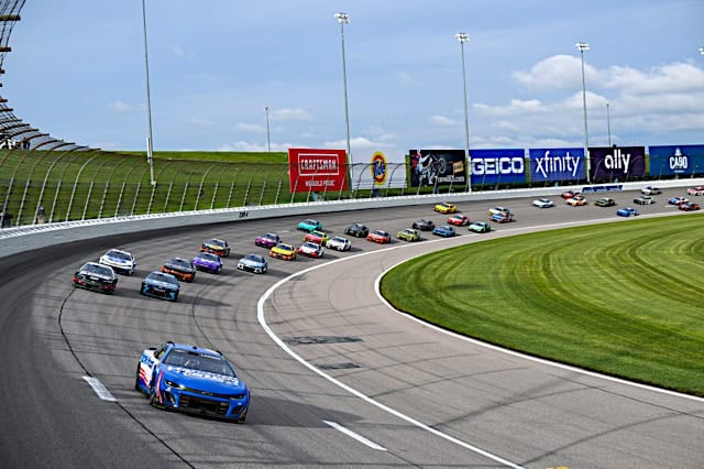 Nascar Cup Series car of Kyle Larson leading a pack of cars around a turn at Kansas Speedway, NKP