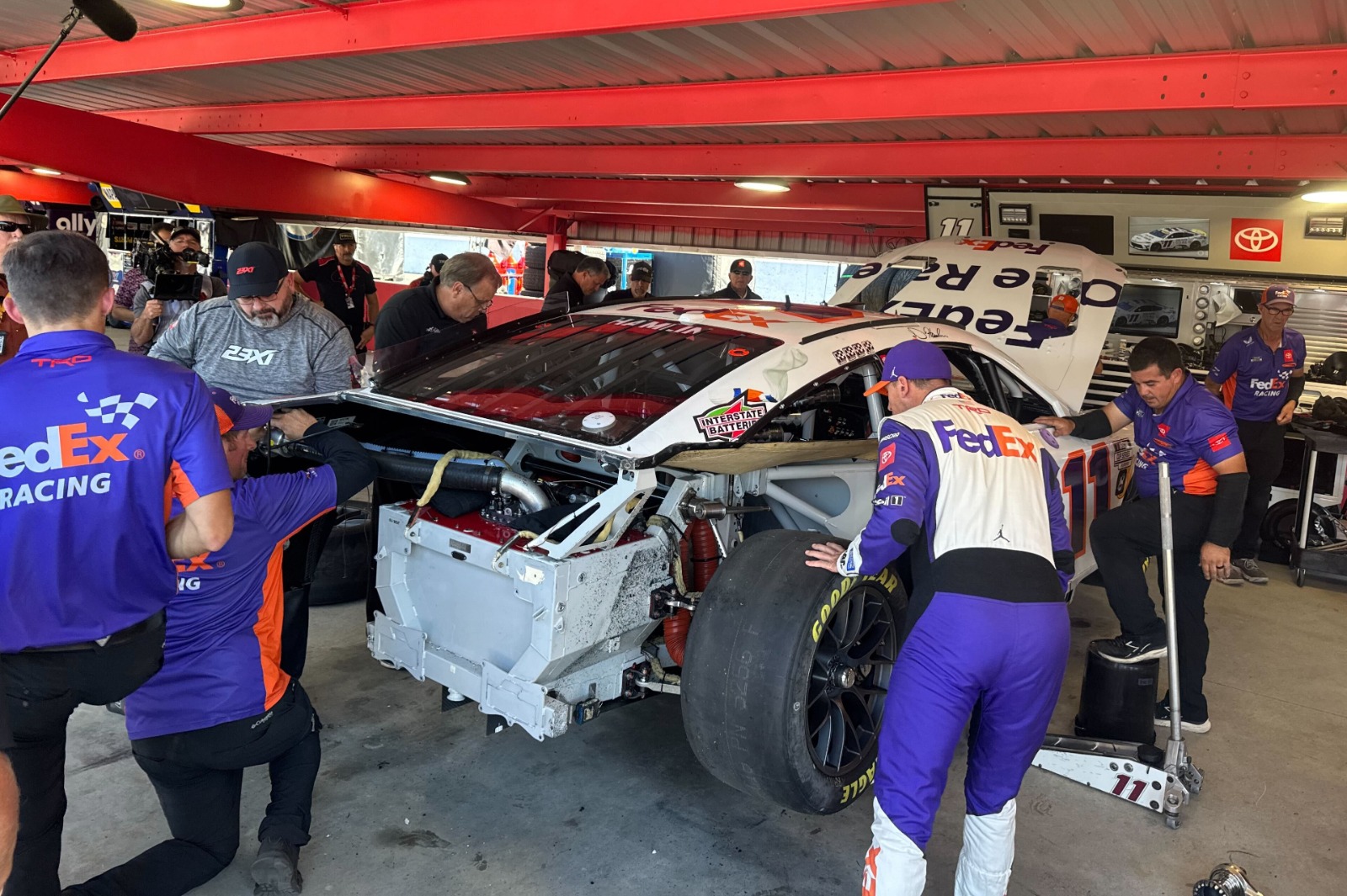 Denny Hamlin takes a look at the damage on the No. 11 while JGR and 23XI crew members continue to disassemble the car.